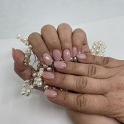 Manos cogiendo unas perlas y con la manicura en color nude.